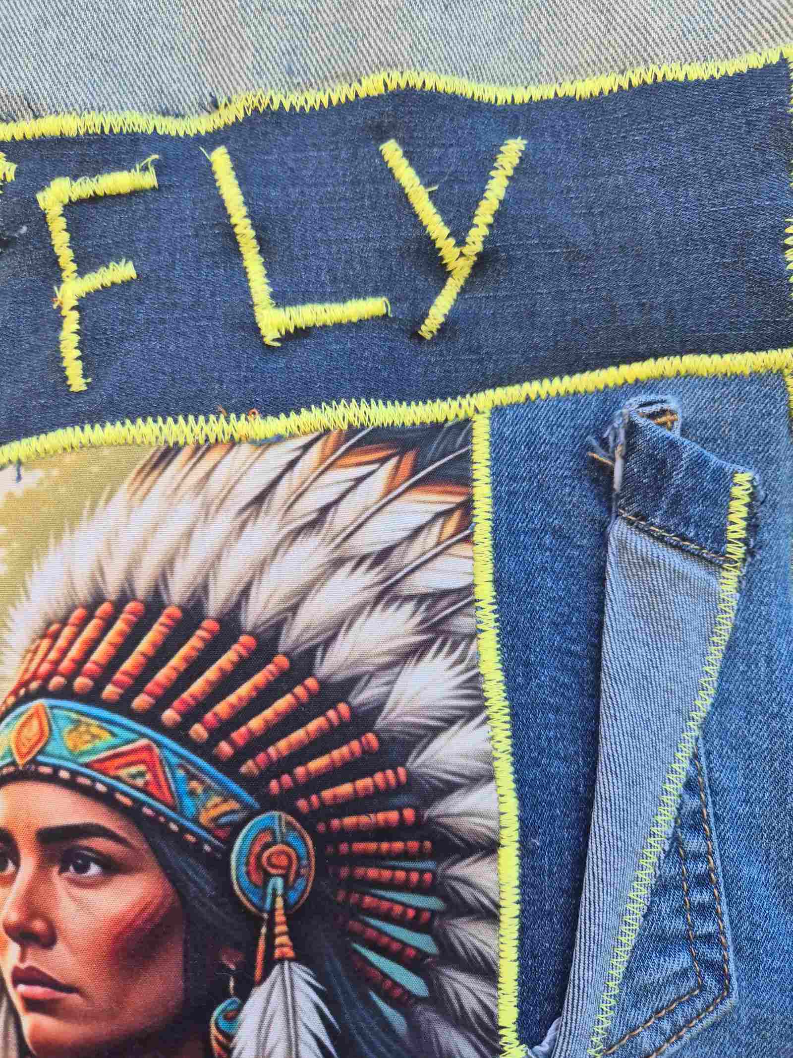 Detailfoto van Fly artwork en neon stiksel op upcycled denim
