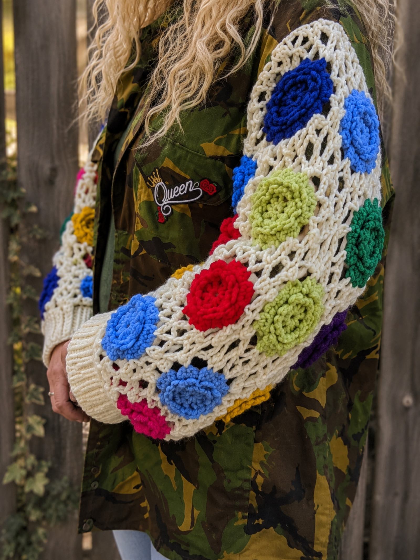 Close-up van handgehaakte kleurrijke bloemenmouwen op een unieke upcycled camouflage jas.
