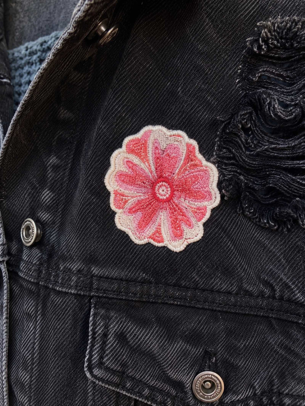 Detailfoto van een roze geborduurde bloemenpatch op een zwart distressed denim jasje van Old New Atelier.