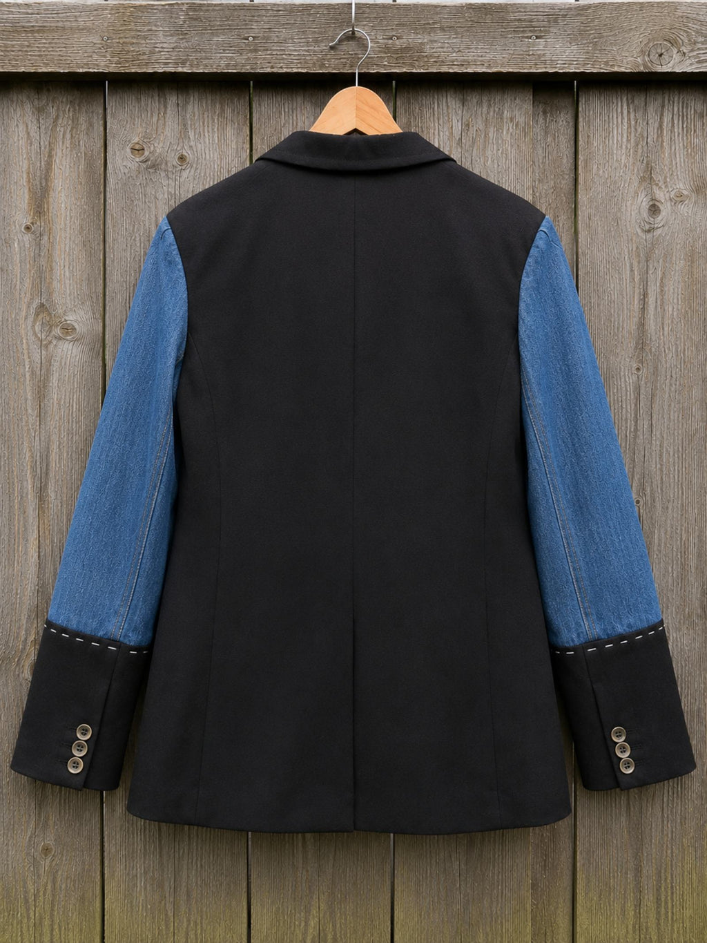 Achterzijde van een handgemaakt upcycled denim colbert op hanger met klassieke zwarte afwerking