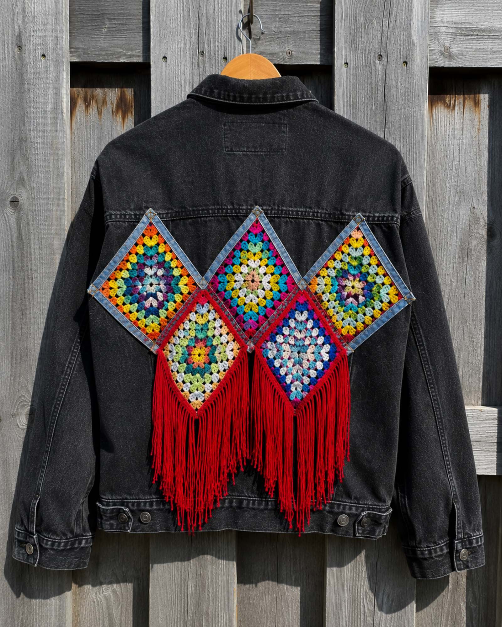 Achterkant van One of a Kind zwart denim jasje met kleurrijk gehaakt kunstwerk en rode franjes op hanger.