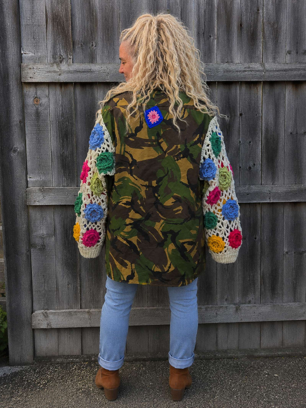 Achterkant van een handgemaakte camouflage jas met kleurrijke gehaakte bloemenmouwen, oversized boho stijl.