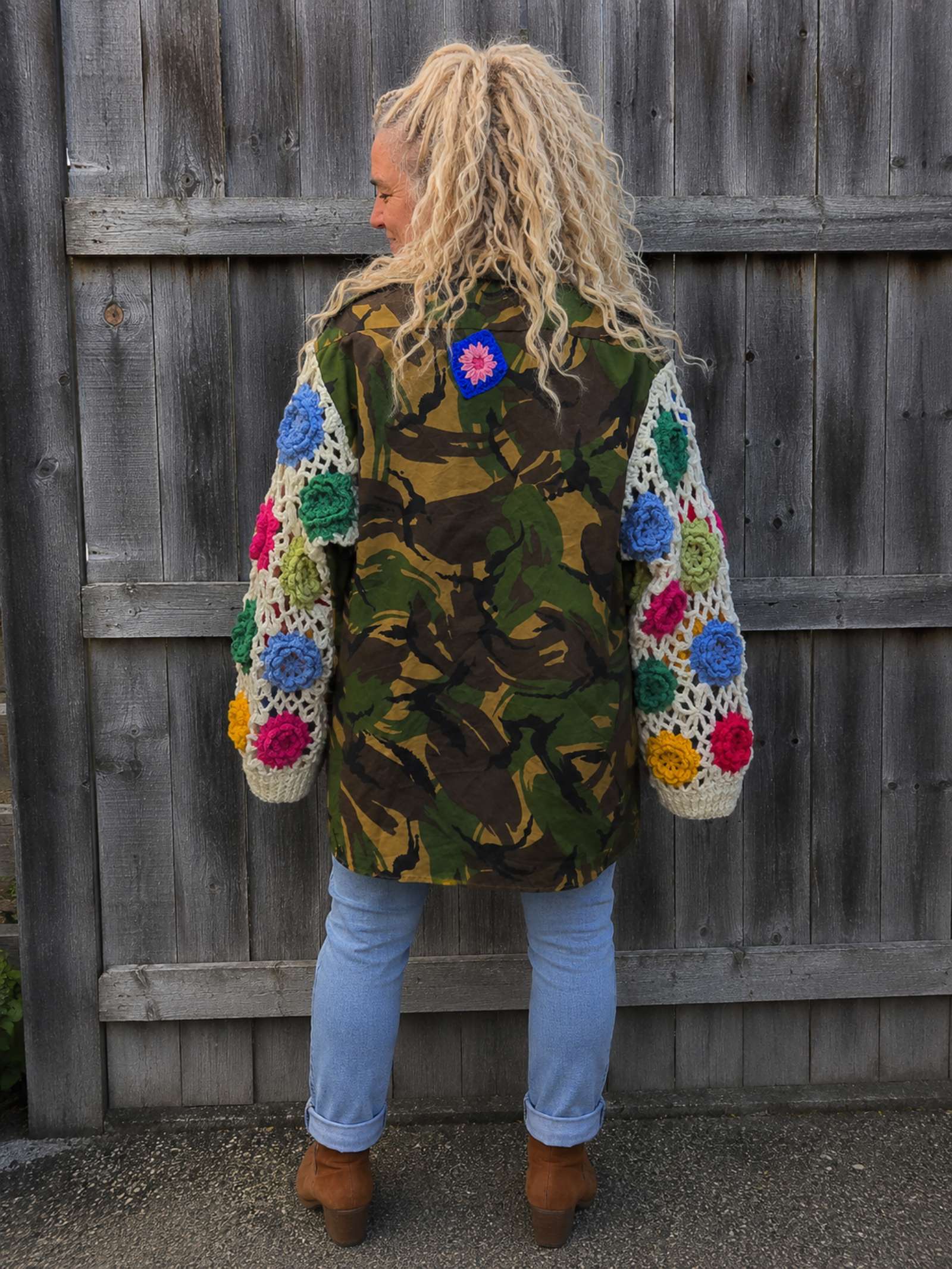 Achterkant van een handgemaakte camouflage jas met kleurrijke gehaakte bloemenmouwen, oversized boho stijl.