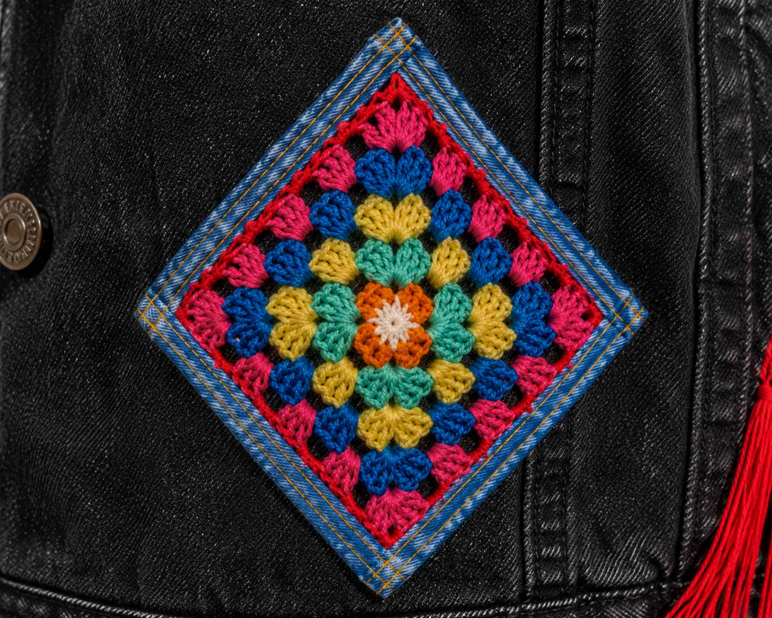 Close-up van de gehaakte granny square applicatie op de voorkant van het zwarte denim jasje.
