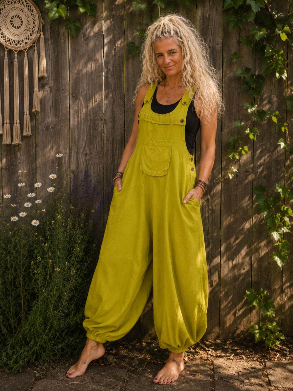Limegroene boho harem jumpsuit gedragen met zwart mouwloos topje, blote voeten en wijde harembroek in zomerse tuin.