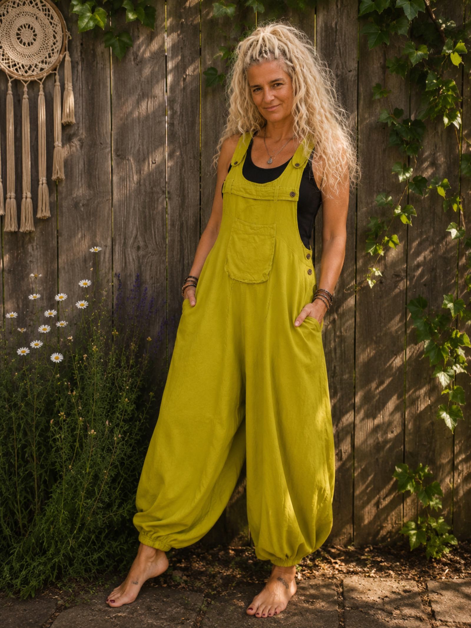 Limegroene boho harem jumpsuit gedragen met zwart mouwloos topje, blote voeten en wijde harembroek in zomerse tuin.