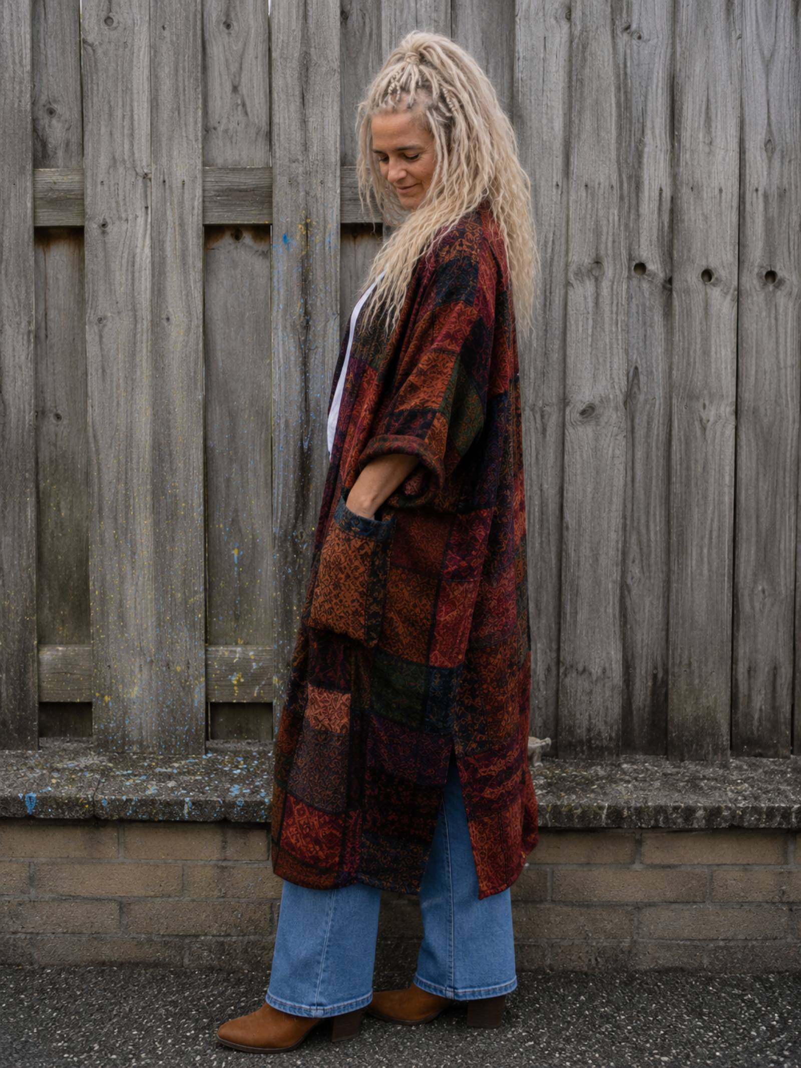 Zijaanzicht van een vrouwelijk model met hand in de zak van een oversized boho patchwork vest in one size aan een houten schutting, Old New Atelier.