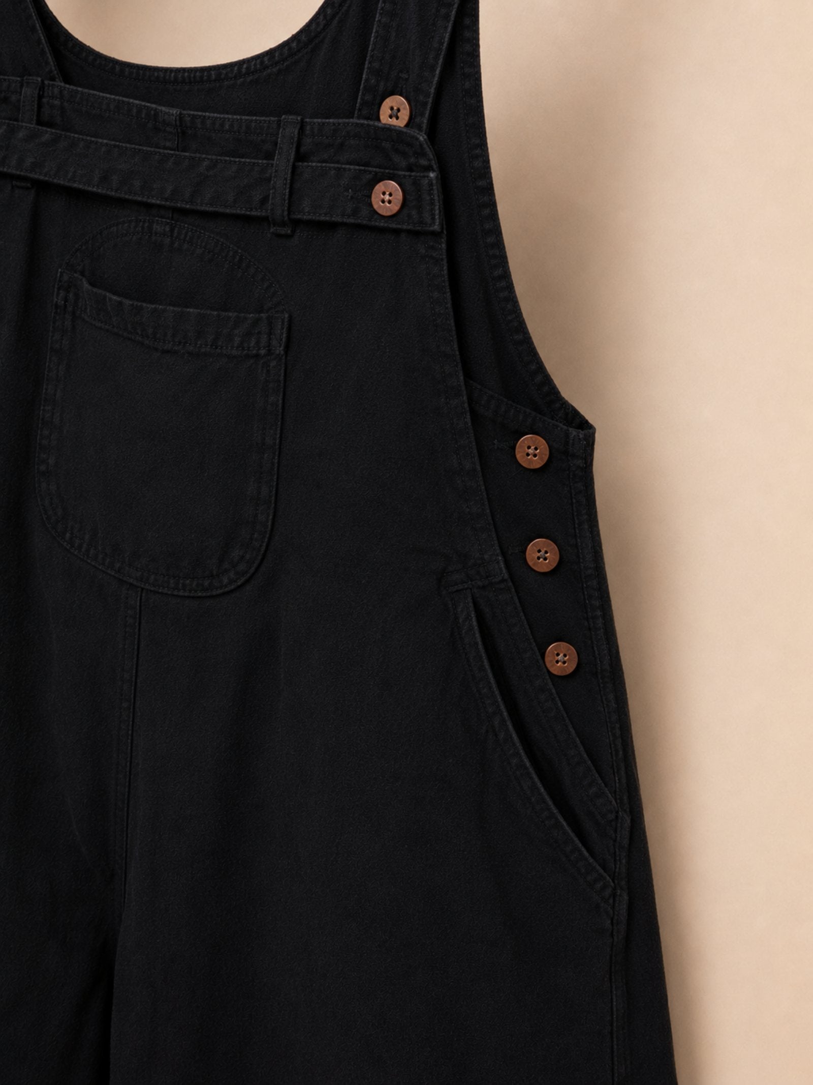 Detail van de verstelbare zijknopen op de zwarte boho tuinbroek voor extra draagcomfort.