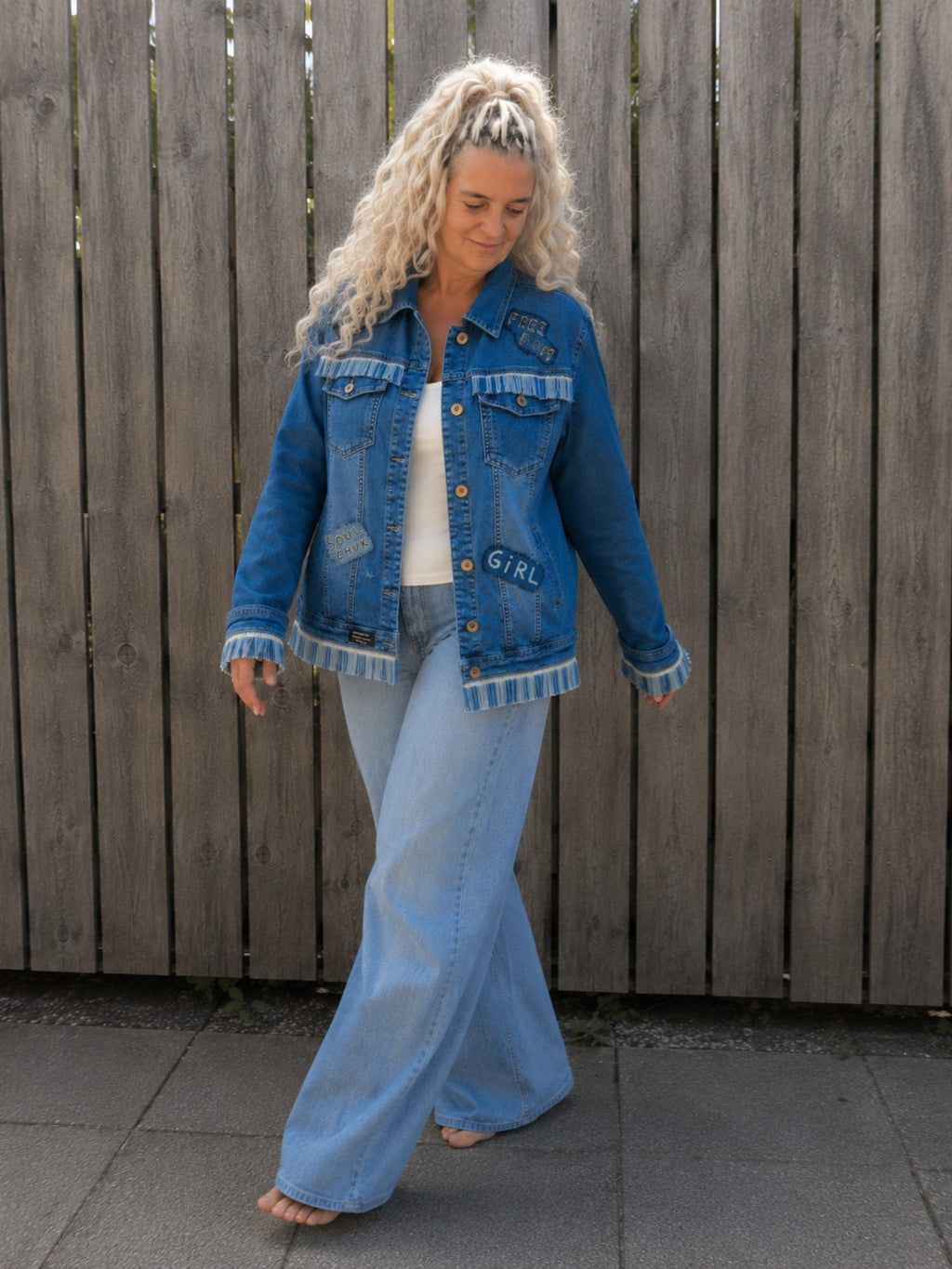 Model draagt One of a Kind upcycled denim jasje met franjes tijdens een ontspannen wandeling buiten