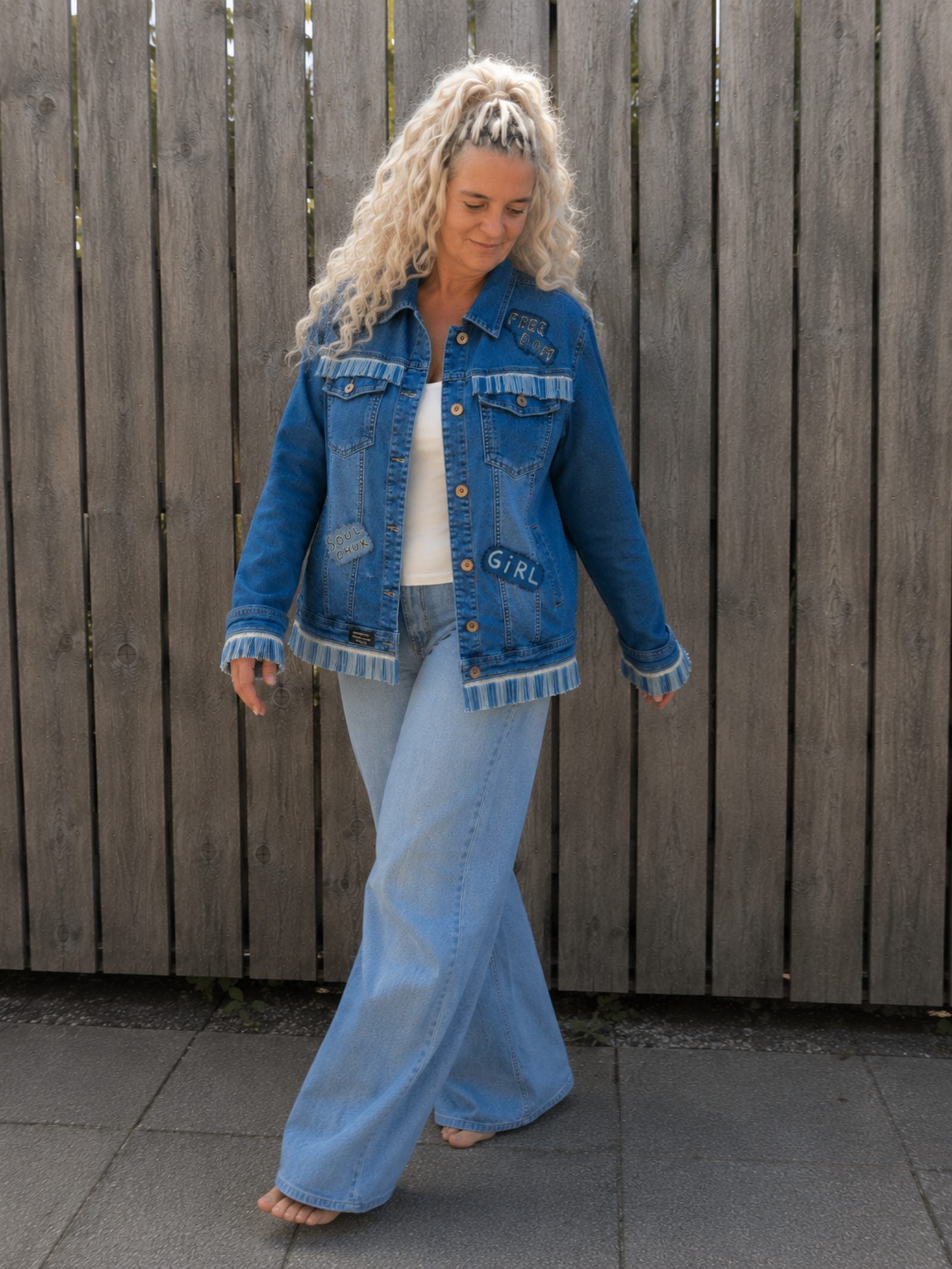 Model draagt One of a Kind upcycled denim jasje met franjes tijdens een ontspannen wandeling buiten