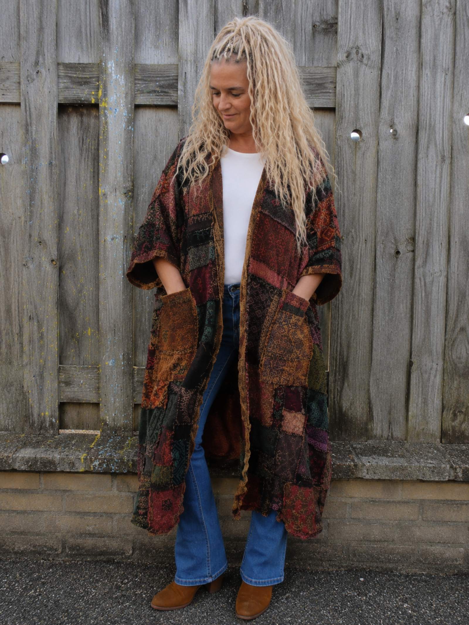 Vrouwelijk model van 1.60 m draagt een oversized boho patchwork vest in one size aan een houten schutting, voorkant zichtbaar, Old New Atelier.