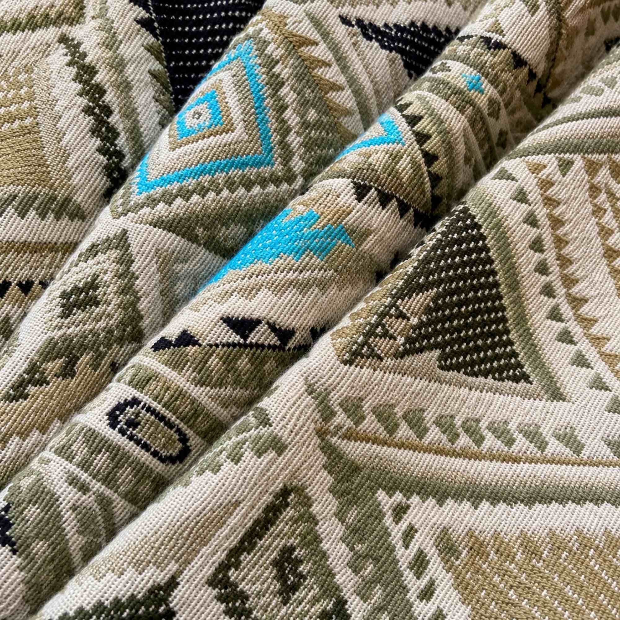 Close-up van de geweven boho stof met turquoise en olijfgroene details van een handgemaakt jasje.