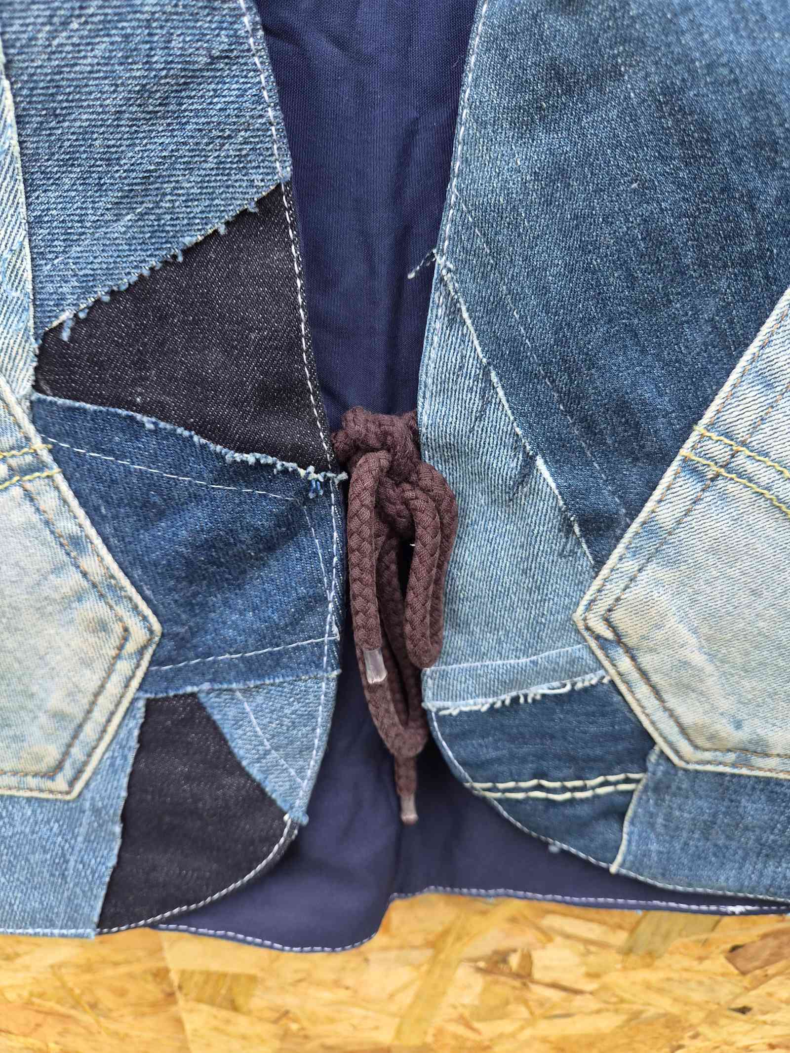 Close-up van de handgemaakte koordsluiting van het One of a Kind upcycled denim patchwork hesje.