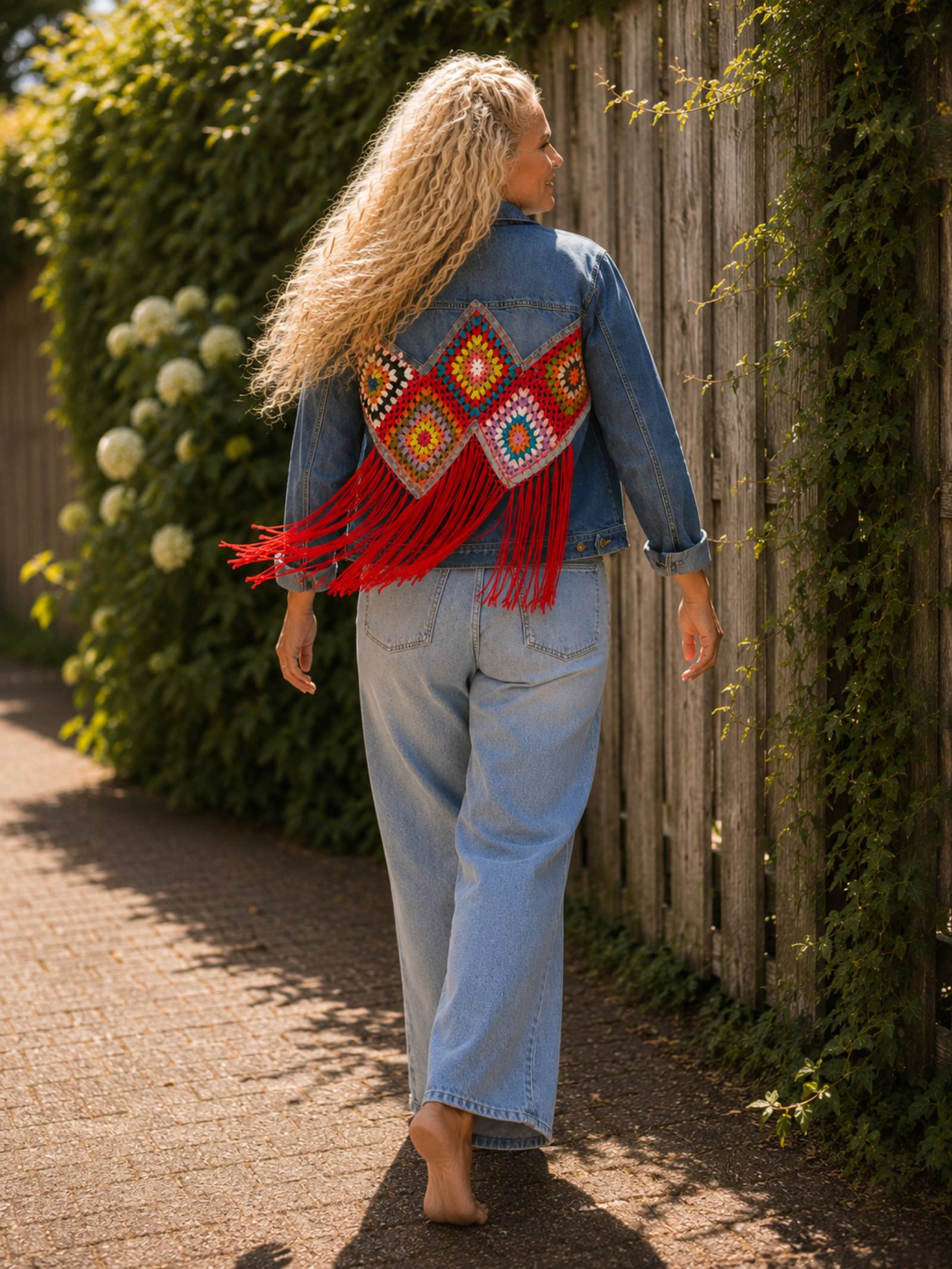 Lopend model draagt handgemaakt upcycled denim jasje met kleurrijke granny squares en bewegende rode franjes.