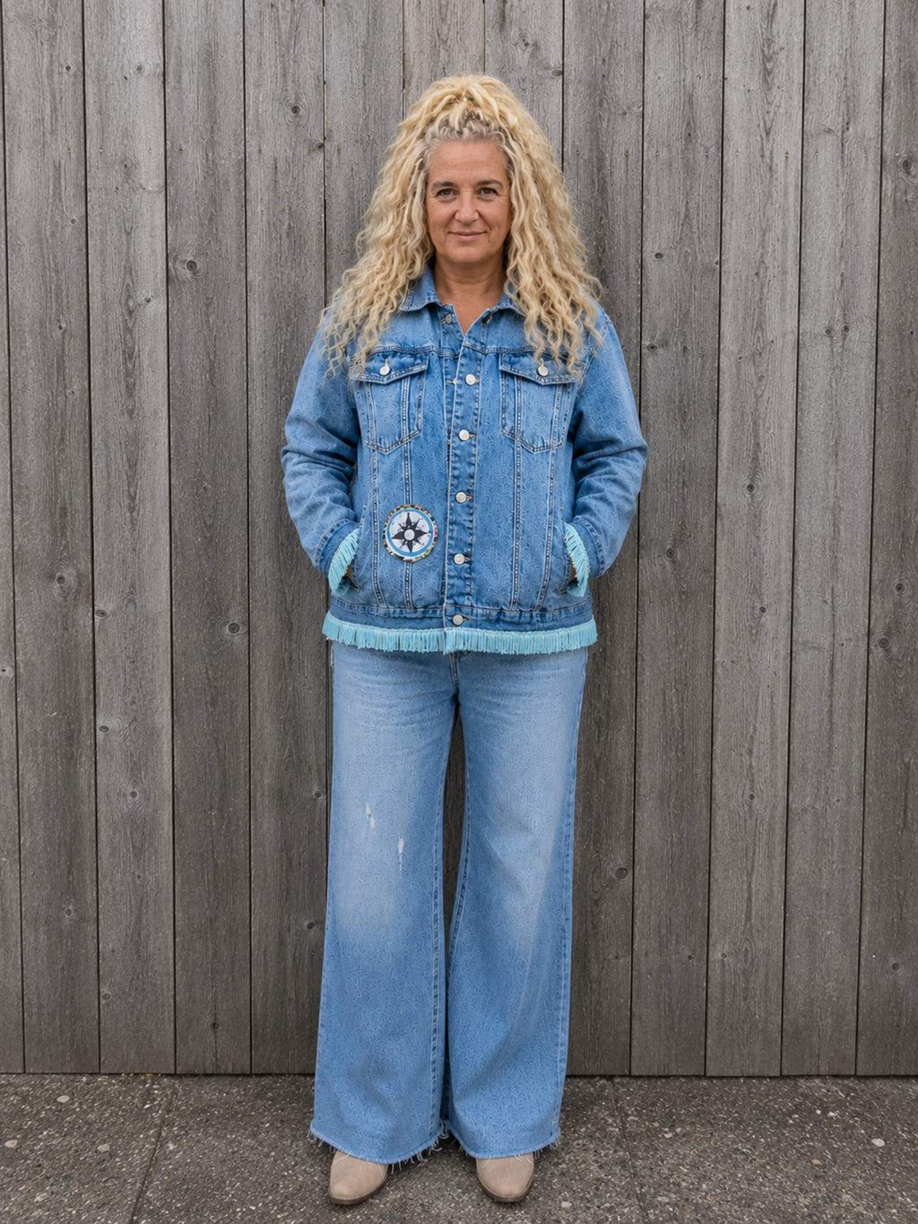 Vrouwelijk model draagt Moon Soul denim jasje met franjes aan houten schutting – One of a Kind Old New Atelier