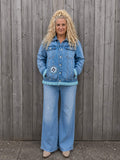 Vrouwelijk model draagt Moon Soul denim jasje met franjes aan houten schutting – One of a Kind Old New Atelier