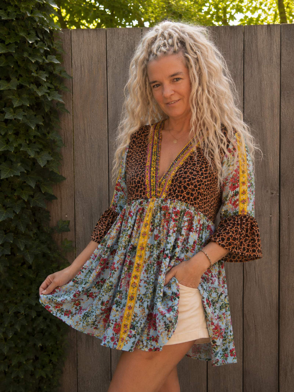 Boho tuniek met bloemenprint in een schuine pose, gedragen. Zwierige pasvorm met kleurrijke details en geborduurde V-hals.