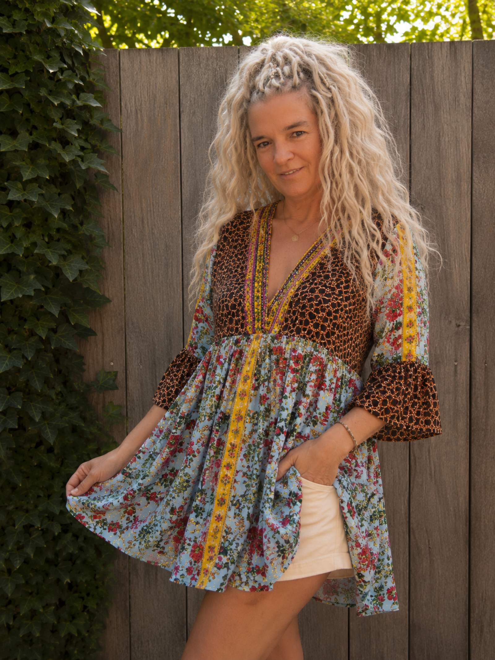 Boho tuniek met bloemenprint in een schuine pose, gedragen. Zwierige pasvorm met kleurrijke details en geborduurde V-hals.