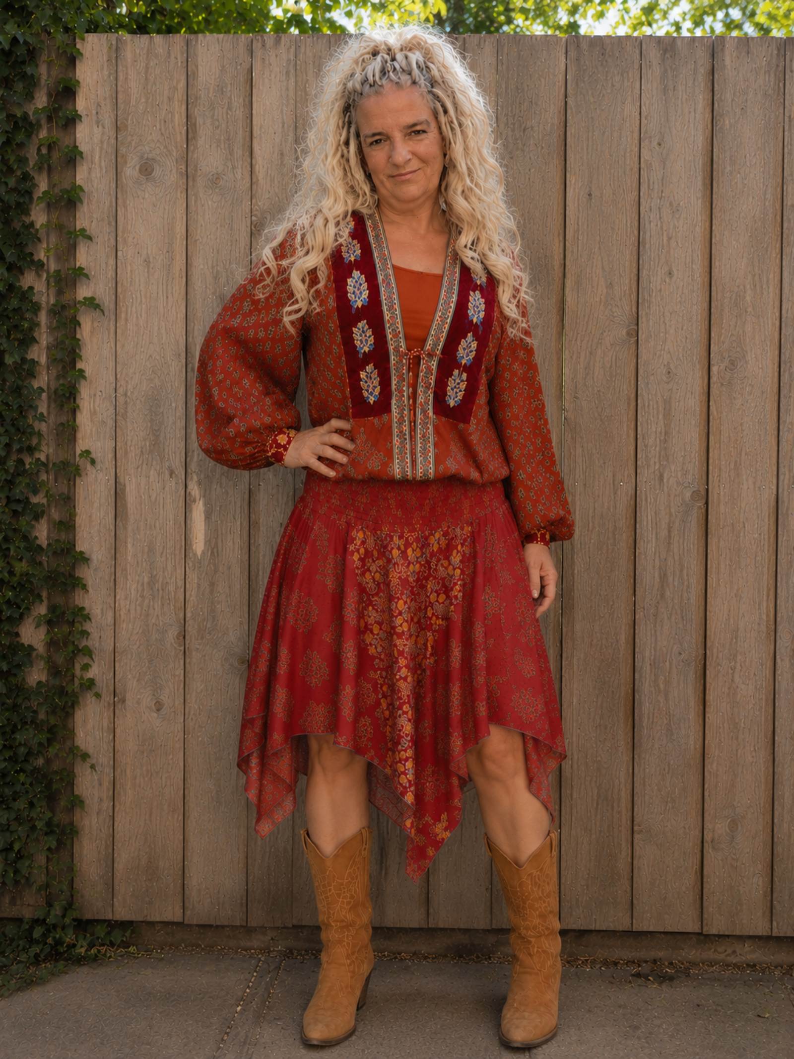Vrouwelijk model draagt een rode asymmetrische boho rok met bijpassend boho blousje en cowboylaarzen. One of a Kind boho look.