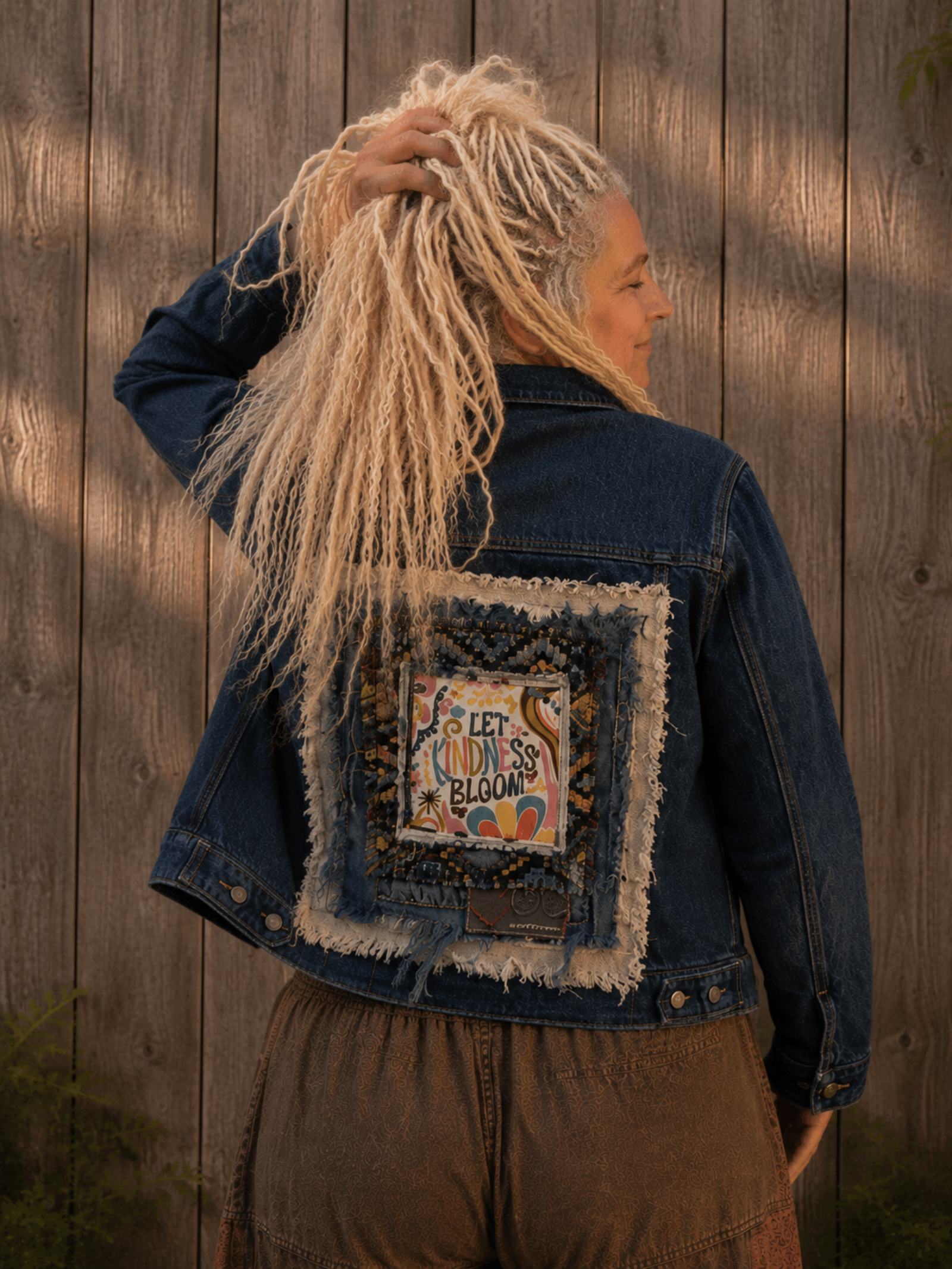 Achterkant van one of a kind upcycled jeansjasje Let Kindness Bloom gedragen door vrouwelijk model met handgemaakte patchwork kunst – Old New Atelier