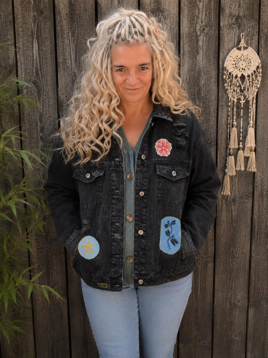 Vrouwelijk model draagt een one of a kind zwart denim jasje met distressed details, bloemenpatch en libellenpatch van Old New Atelier.