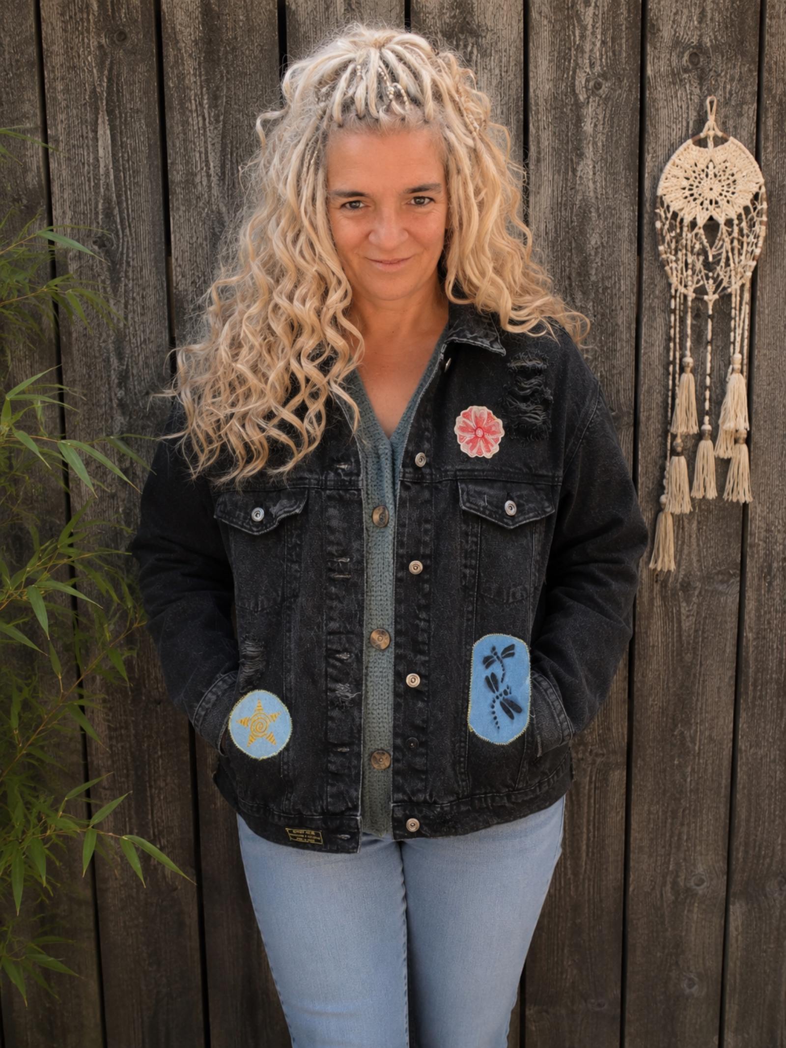 Vrouwelijk model draagt een one of a kind zwart denim jasje met distressed details, bloemenpatch en libellenpatch van Old New Atelier.