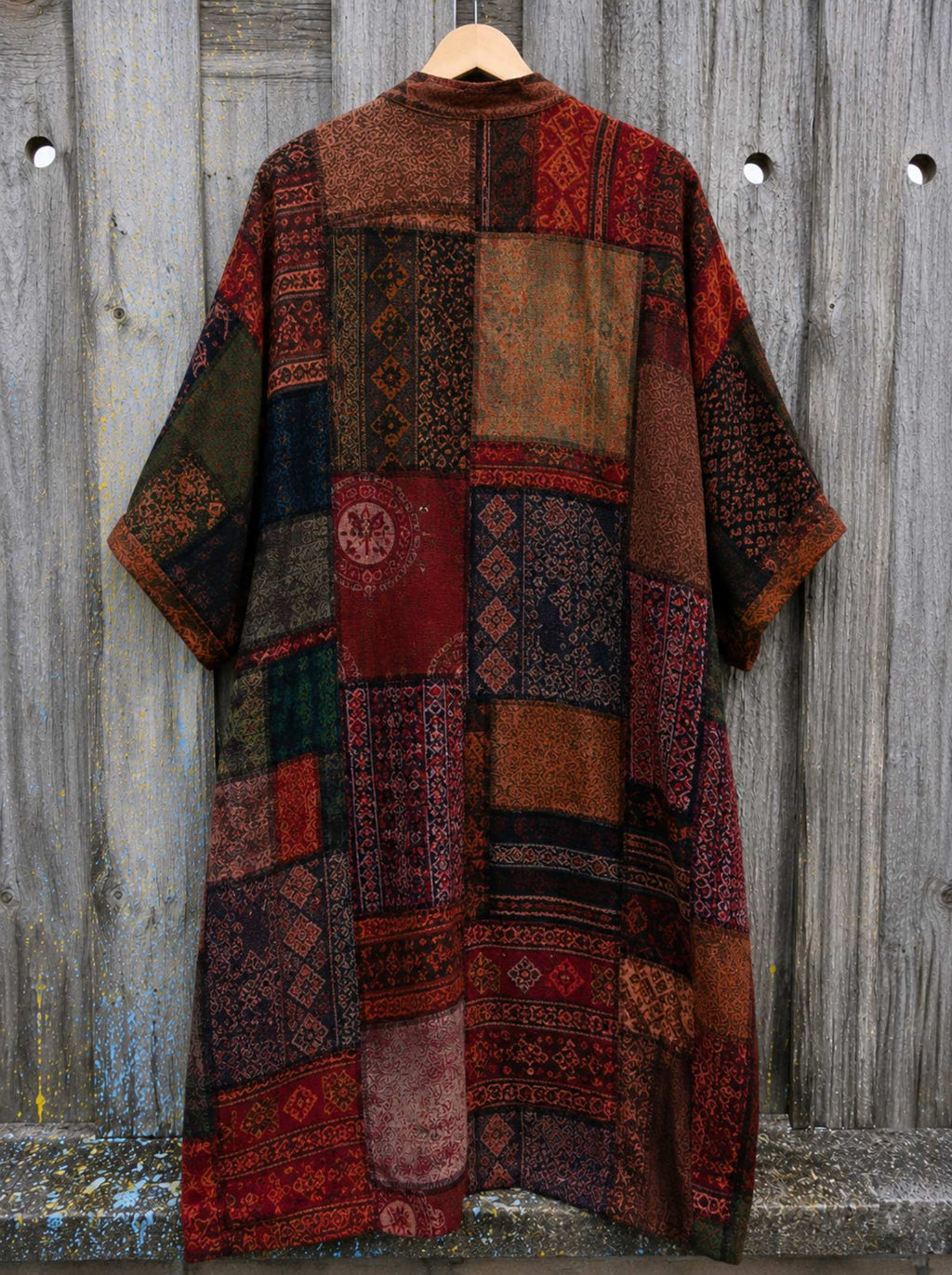 Achterkant van een oversized boho patchwork vest in one size met kleurrijk patchworkpatroon hangend aan een houten schutting, Old New Atelier.