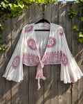 Witte boho wrap top met rode Om symbolen hangend aan houten schutting – luchtige festival stijl