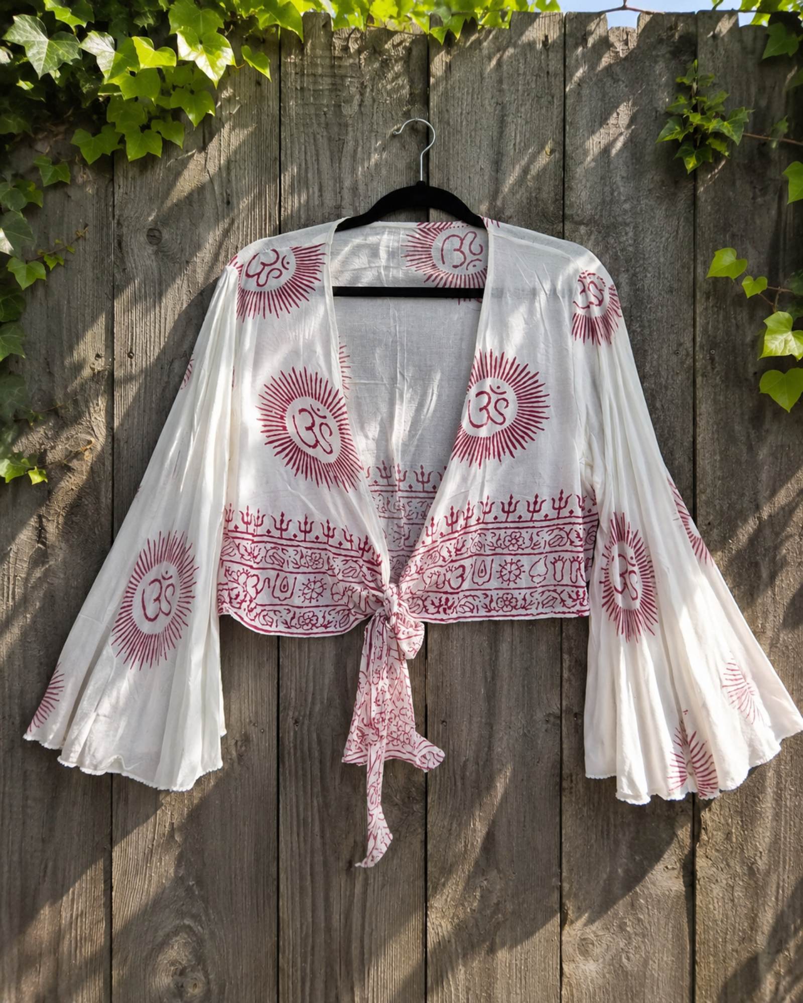 Witte boho wrap top met rode Om symbolen hangend aan houten schutting – luchtige festival stijl